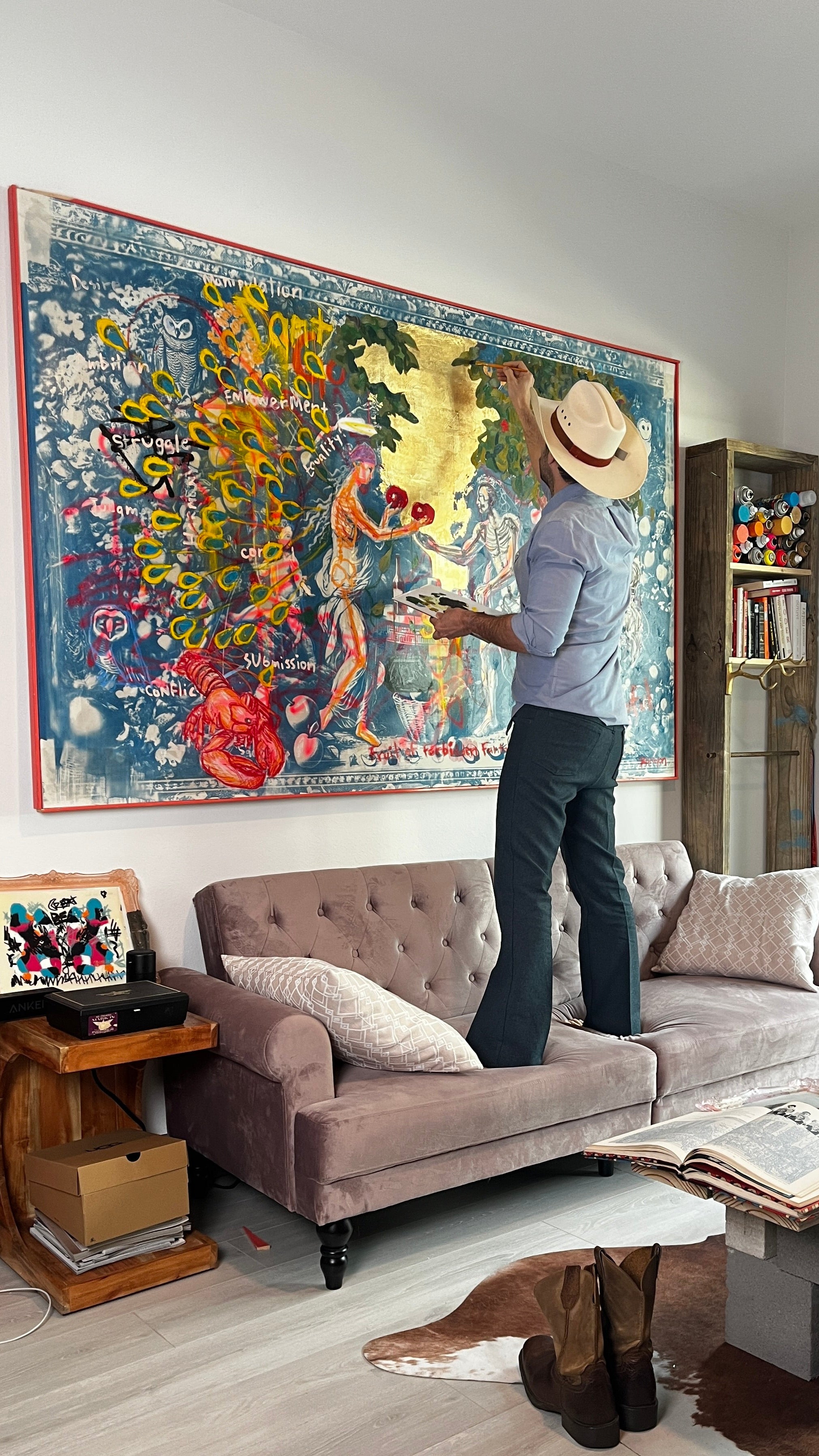 Papayon standing on a couch painting at a large colorful painting in a living room.